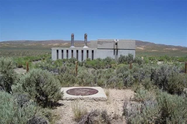 An above-ground concrete structure amid scrubland under a clear blue sky.