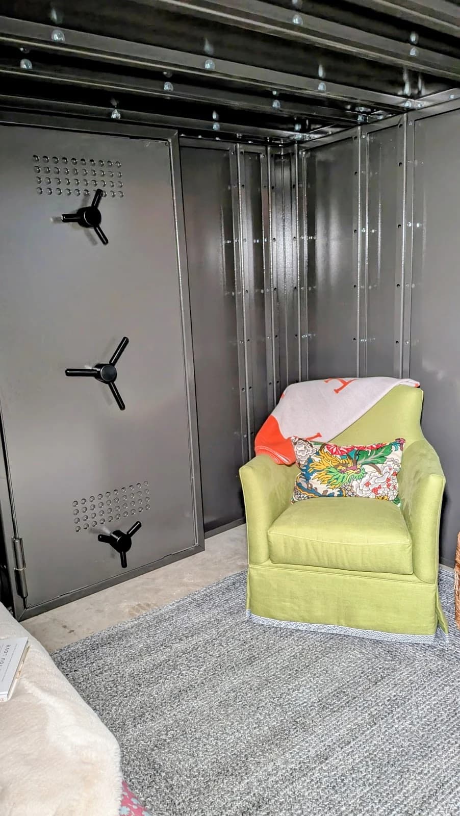 A steel safe-room interior with a vault door and a green armchair.